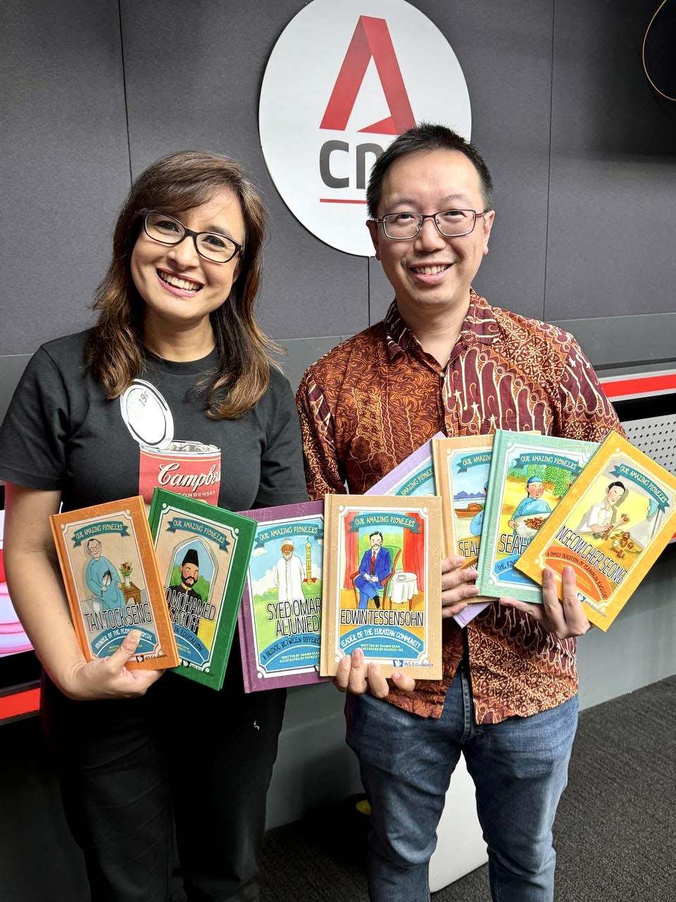 Shawn Seah holding up copies of Our Amazing Pioneers with CNA radio personality. 