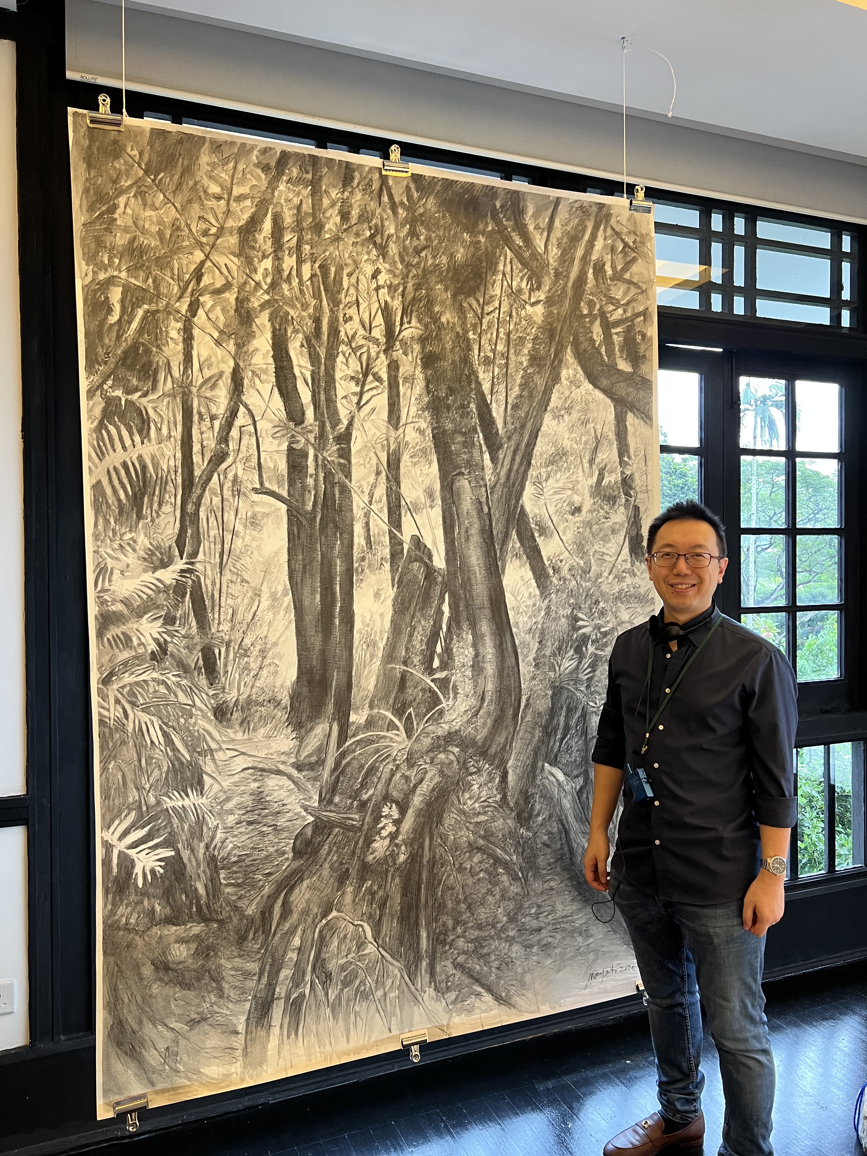 Published author and public speaker Shawn Seah standing in front of a large charcoal drawing, in a colonial-era bungalow. 