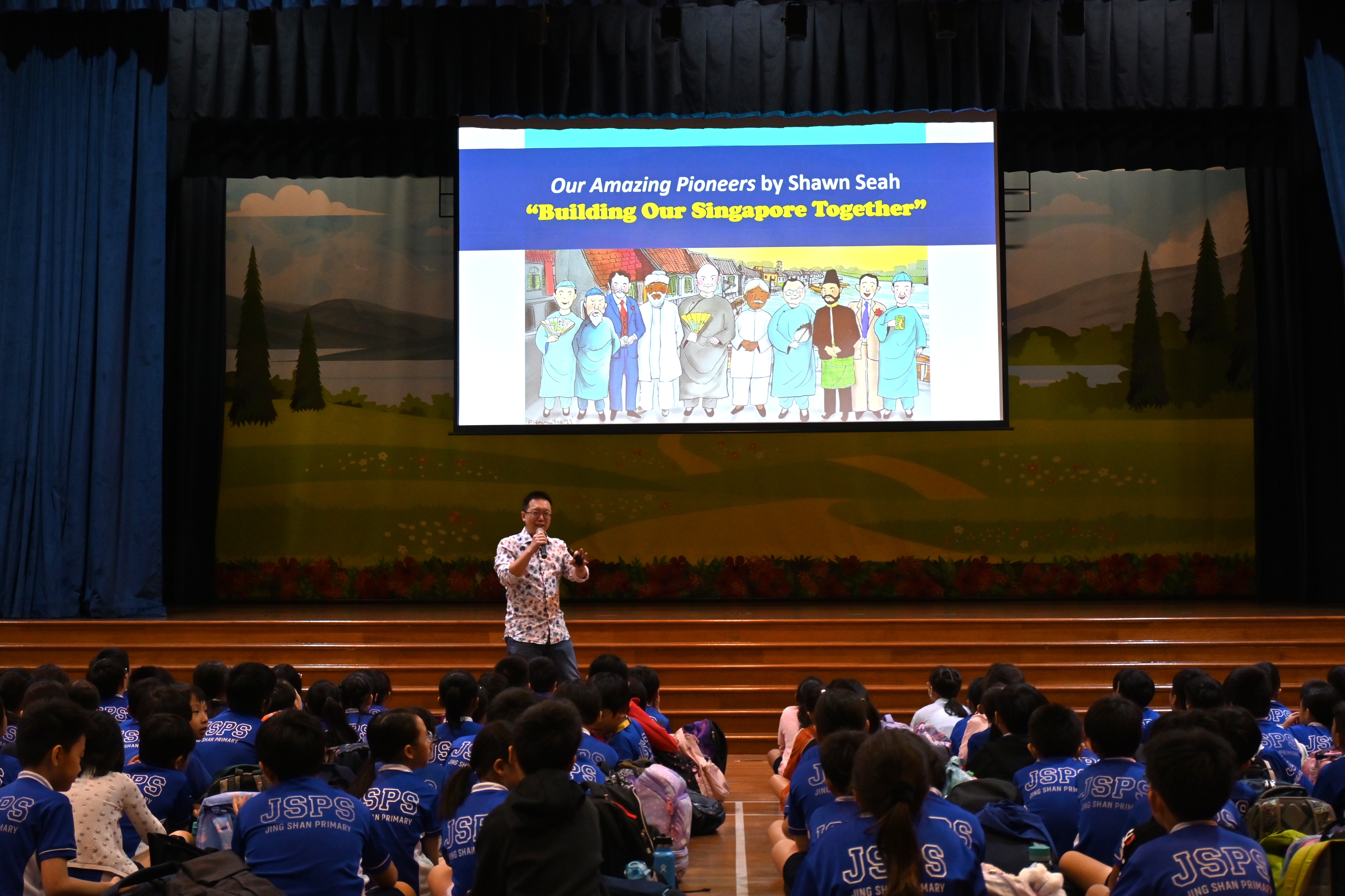 Author Shawn Seah speaking to primary school pupils at a morning assembly talk in a school hall.